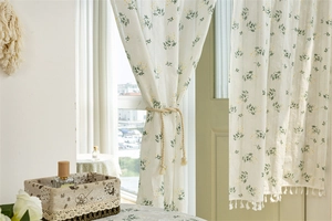 Detail of floral printed cotton curtain featuring green leaves and white tassel edges