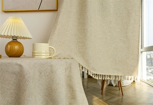 Close-up detail of beige linen door curtain with decorative tassel fringe edges