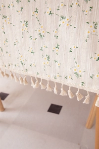 Detail of floral jacquard cotton tablecloth featuring daisy embroidery and tassel trim