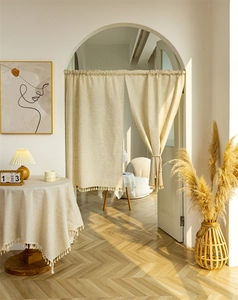 Detail of beige linen door curtain with handmade fringe trim in natural sunlight