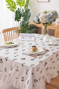 Detail of white cotton tablecloth featuring black floral embroidery and ruffled edges