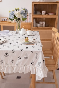 Detail of white cotton tablecloth with black floral embroidery and ruffled edges in a cozy room