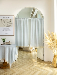 Detail of light blue striped cafe curtain with beige tassels in a bright French country setting