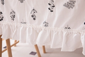 Detail view of cotton tablecloth featuring black floral embroidery and elegant ruffles