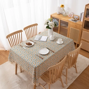 Rectangular tablecloth with orange fruit print and tassel trim on a wooden dining table