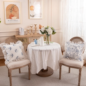 Detail of French floral cushion with ruffled edges and white lace tablecloth on a wooden cabinet