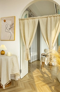 Detail of beige linen door curtain with tassels and matching tablecloth in warm sunlight