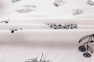 Macro detail of white cotton fabric with black floral embroidery and textured ruffle edges