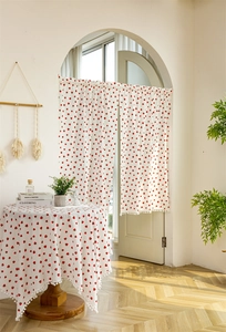Detail of strawberry print cotton curtain and round tablecloth with white pompom fringe