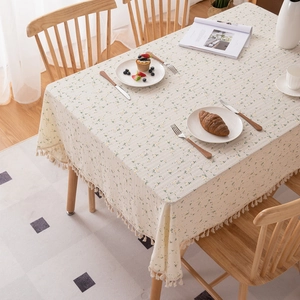 Cream floral cotton tablecloth with sunflower print and tassels on a wooden table