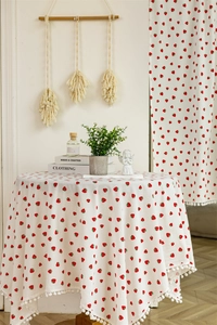 Close-up of a white cotton round tablecloth with red strawberry prints and pom-pom trim