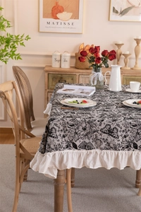 Detailed texture of black floral butterfly patterns and cream ruffled cotton tablecloth edge