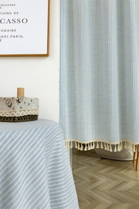 Detail showing blue and white striped cotton fabric curtain with beige tassel trim decor