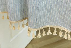 Detail of blue and white vertical striped cotton curtain with elegant cream fringe tassels