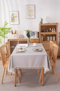 Detail of light grey waterproof PVC tablecloth featuring elegant cream tassel edges and natural drape