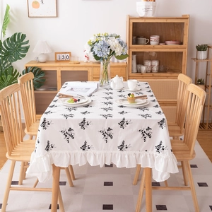 White cotton tablecloth with black floral embroidery and ruffled edges in home setting