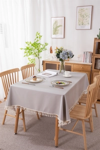 Detail of grey waterproof PVC tablecloth with white tassels in a Nordic dining setting