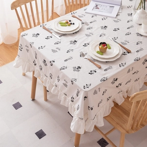 White cotton tablecloth with black floral embroidery and elegant ruffled edges on wood table