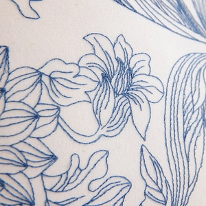 Detailed close-up of blue floral embroidery on ruffled cream cotton pillow cover fabric