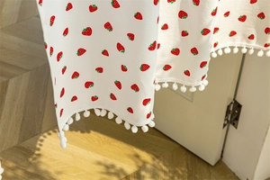 Detail of cream cotton door curtain featuring red strawberry prints and pom-pom trim