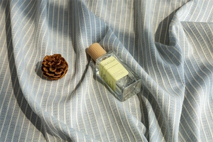 Close-up of 50ml cologne glass bottle with wooden cap on blue striped linen fabric