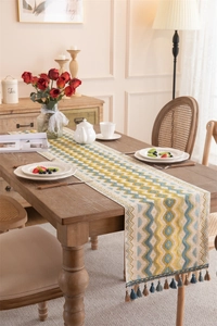 Detail of woven geometric table runner with blue tassels on a wooden dining table