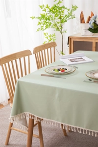 Detail of light green PVC tablecloth with white tassel edges on a wooden dining table