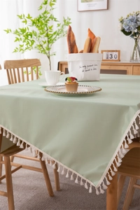 Close-up of light green PVC tablecloth with white tassels on a wooden dining table