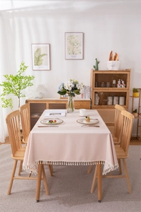 Detail of soft pink PVC tablecloth featuring cream cotton tassels on a wooden dining table