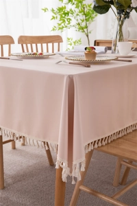 Detail of pink PVC tablecloth with white tassel fringe in a cozy home setting