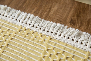 Détail d'une nappe tissée jaune et blanc avec glands décoratifs sur bois naturel