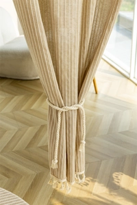 Detail of beige cotton linen striped curtain with tassel trim and woven rope tieback