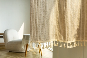 Detail of beige striped cotton linen door curtain with fringe trim in sunlit room
