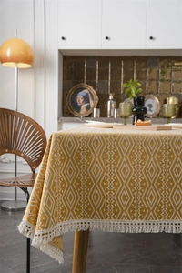 Detalle del patrón jacquard geométrico y flecos blancos en el mantel color amarillo mostaza