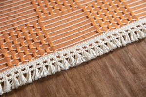 Gros plan sur la nappe jacquard orange avec des détails de franges et de pompons blancs