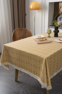 Detalle de mantel geométrico amarillo con rombos de jacquard y borlas blancas