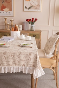 Detail of floral printed beige tablecloth with white pleated ruffle edge and cotton linen texture