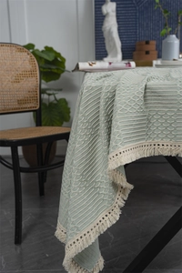 Vue détaillée de la nappe géométrique vert sauge avec élégants pompons de couleur crème