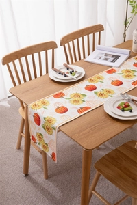 Detail of harvest pumpkin and sunflower table runner on light wooden dining table