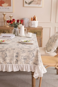 Detail of French floral tablecloth showing blue plant patterns and white ruffled edges