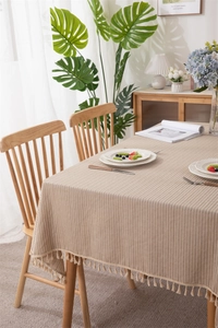 Detailed close-up of light beige cotton jacquard tablecloth with fringe and vertical stripes
