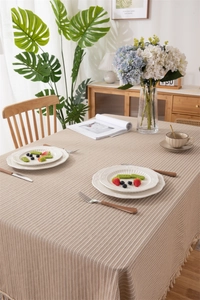 Detailed close-up of beige cotton tablecloth with vertical stripes and tassel trim