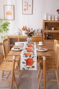 Detail of harvest pumpkin table runner with autumn leaf prints on rustic wooden dining table