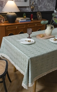 Detalle de mantel bohemio verde con patrones geométricos y bordes de flecos blancos