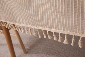 Close-up of beige woven tablecloth featuring vertical stripes and elegant fringe tassels