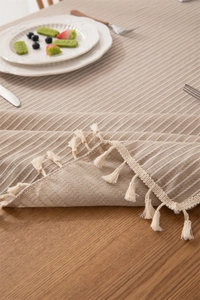 Macro detail of beige cotton jacquard tablecloth with striped texture and fine fringe