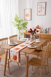 Detail of harvest pumpkin and maple leaf print table runner on wooden dining table