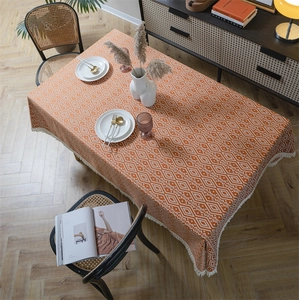 Detalle de patrón geométrico y borlas blancas en el mantel rectangular color naranja