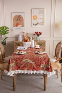 Detail of vintage red cotton tablecloth featuring bird floral prints and white ruffled edges