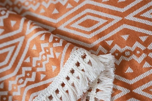 Detalle del mantel de jacquard geométrico con flecos y un patrón de diamantes naranja